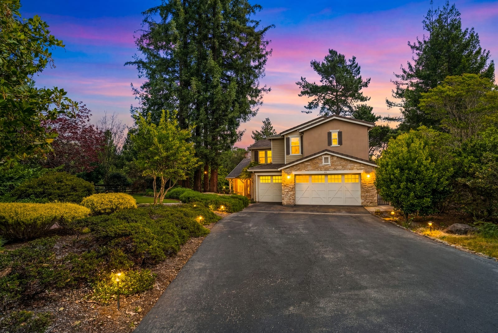 335 Bridlewood Court at twilight, illuminated stone-and-stucco facade beneath a redwood-framed sunset sky
